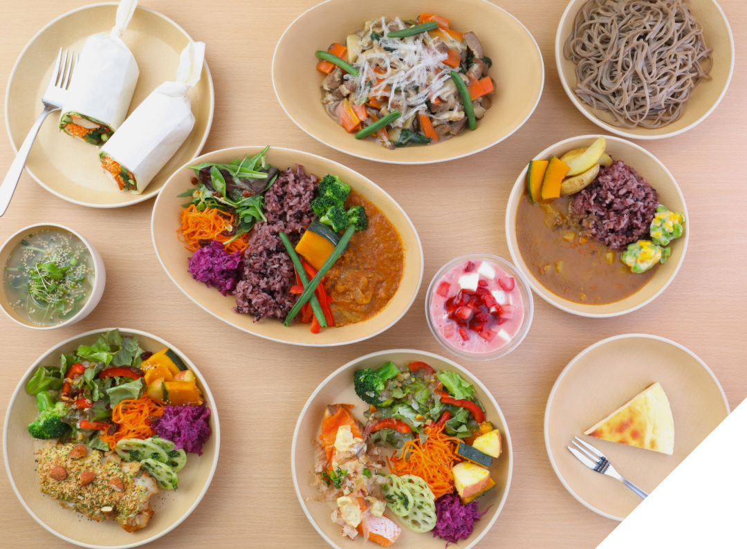 木目調のテーブルに並べられた、カレーやサラダ、蕎麦、デザートなどの彩り豊かなヘルシー料理の数々